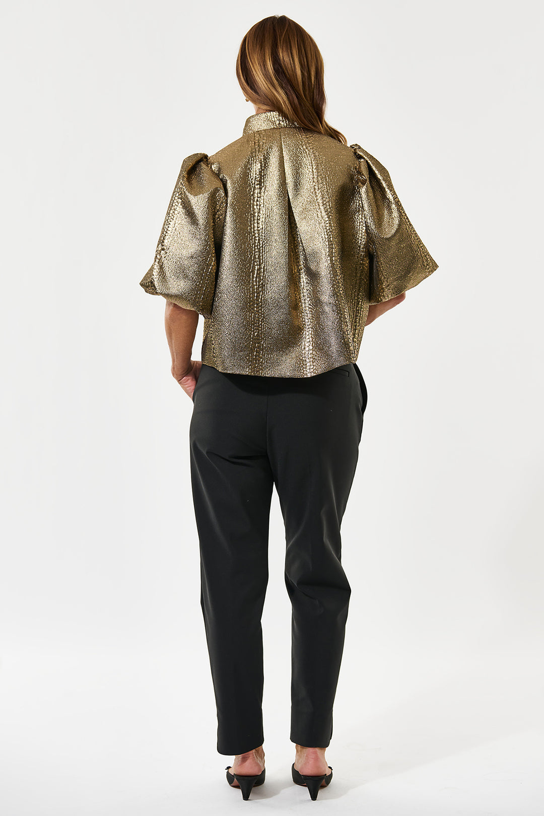 Woman wearing a gold metallic blouse and black pants on a white background