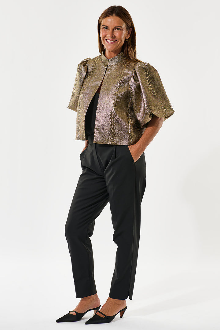 Woman wearing a metallic gold jacket and black pants on a white background
