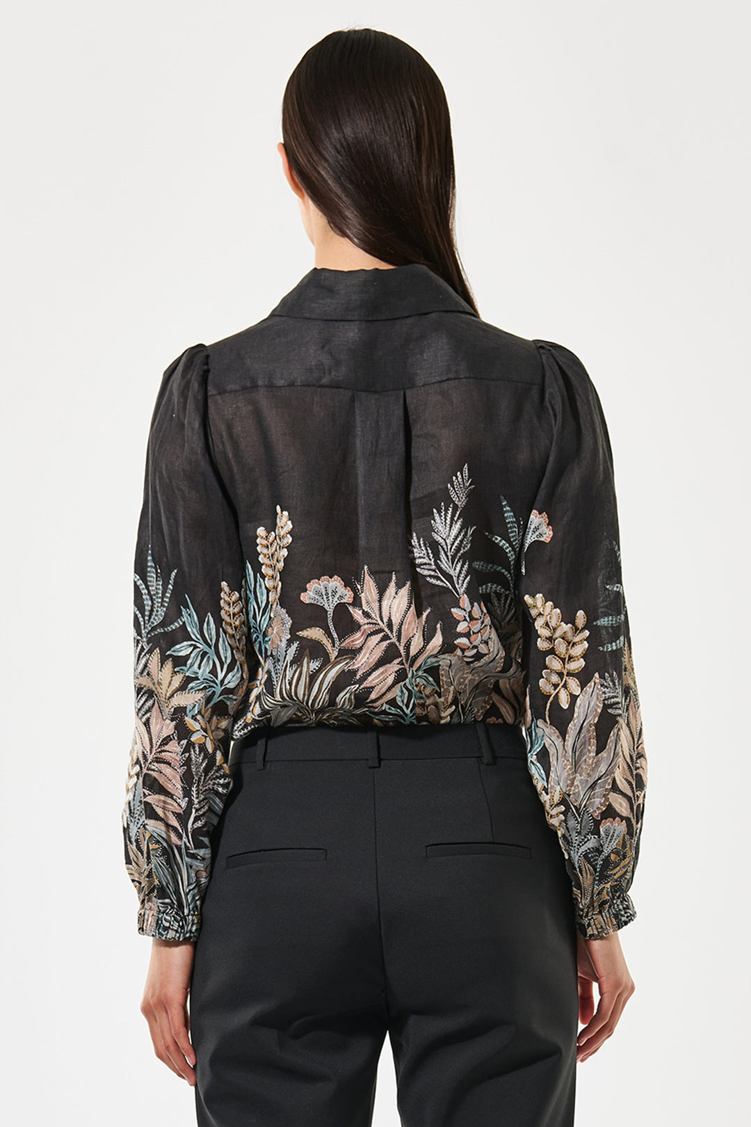 Person wearing a black floral blouse with sheer sleeves on a white background