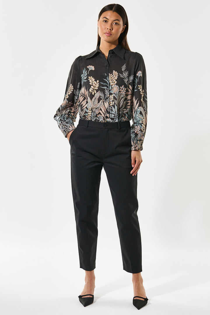 Woman wearing a patterned blouse and black pants on a white background