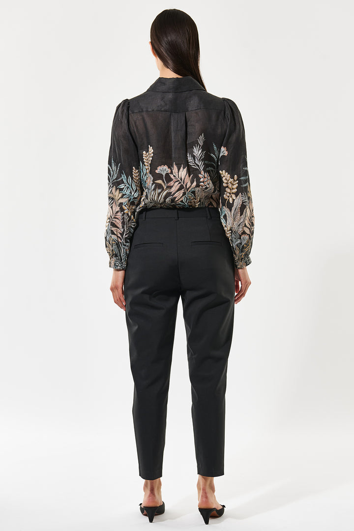 Woman wearing a black floral blouse and black pants on a white background