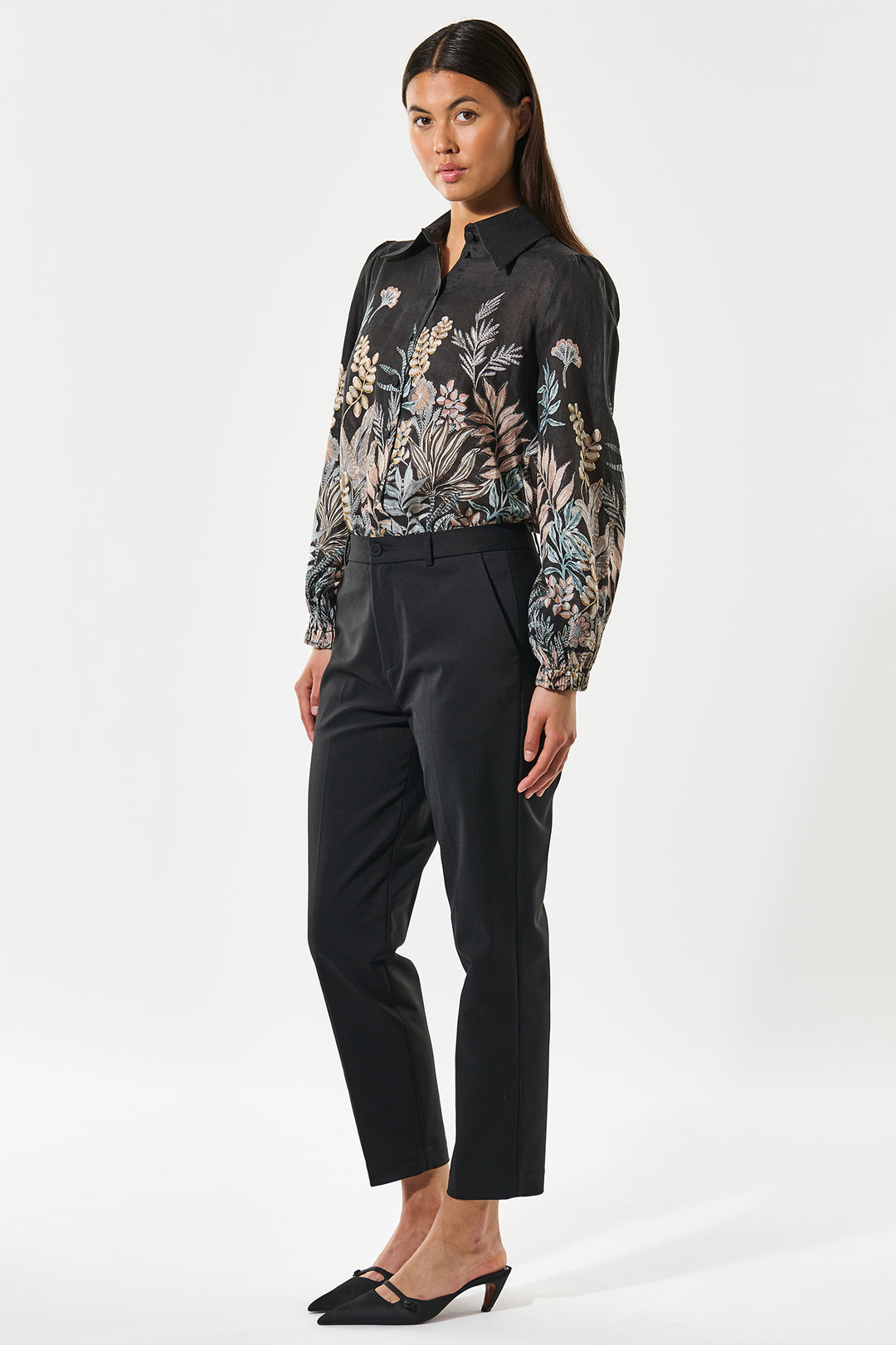 Woman wearing a floral blouse and black pants on a white background