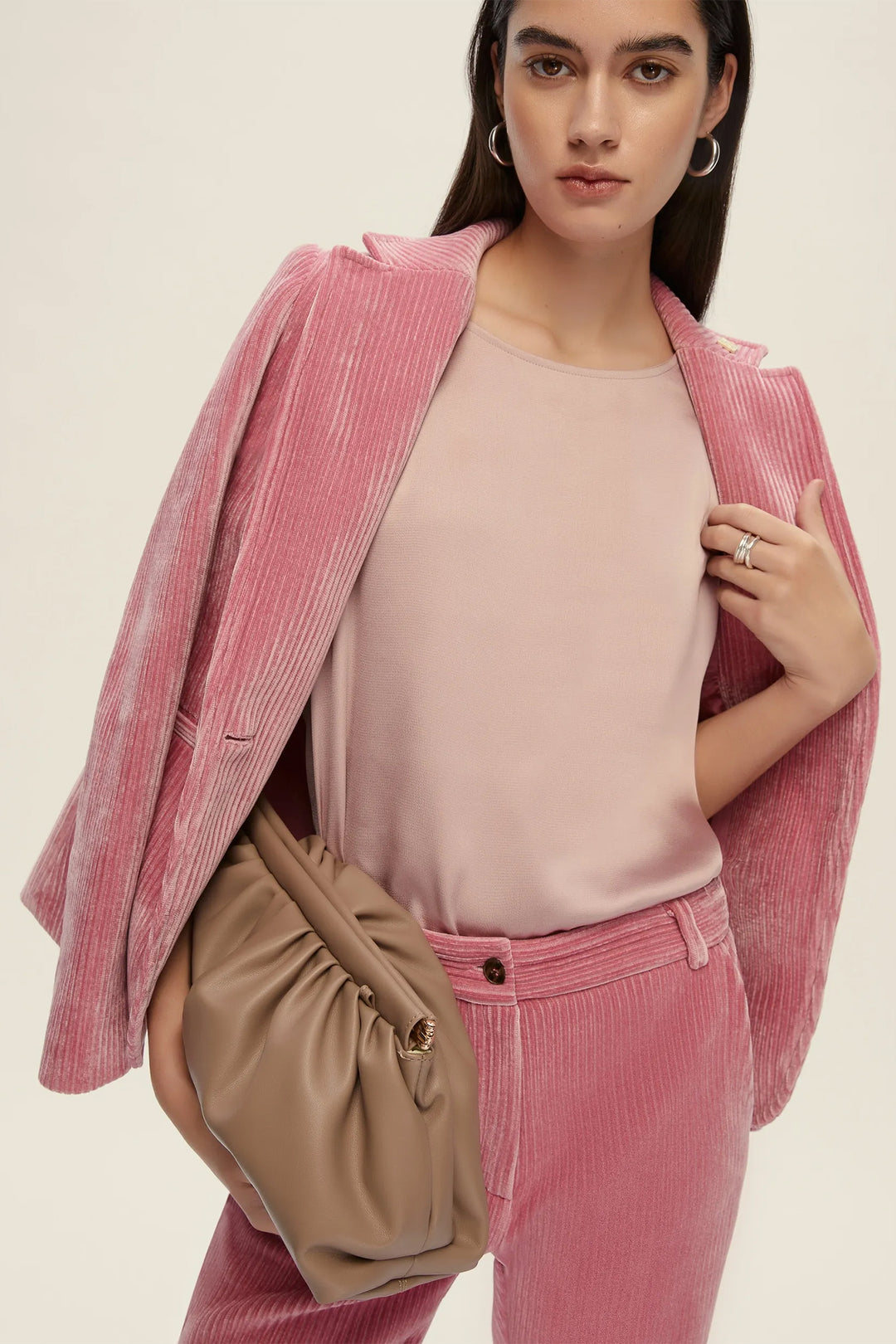 Woman wearing a pink corduroy outfit with a beige bag on a beige background