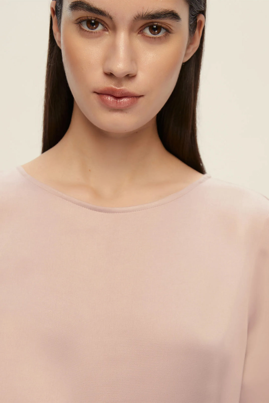 Woman wearing a light pink top against a plain background