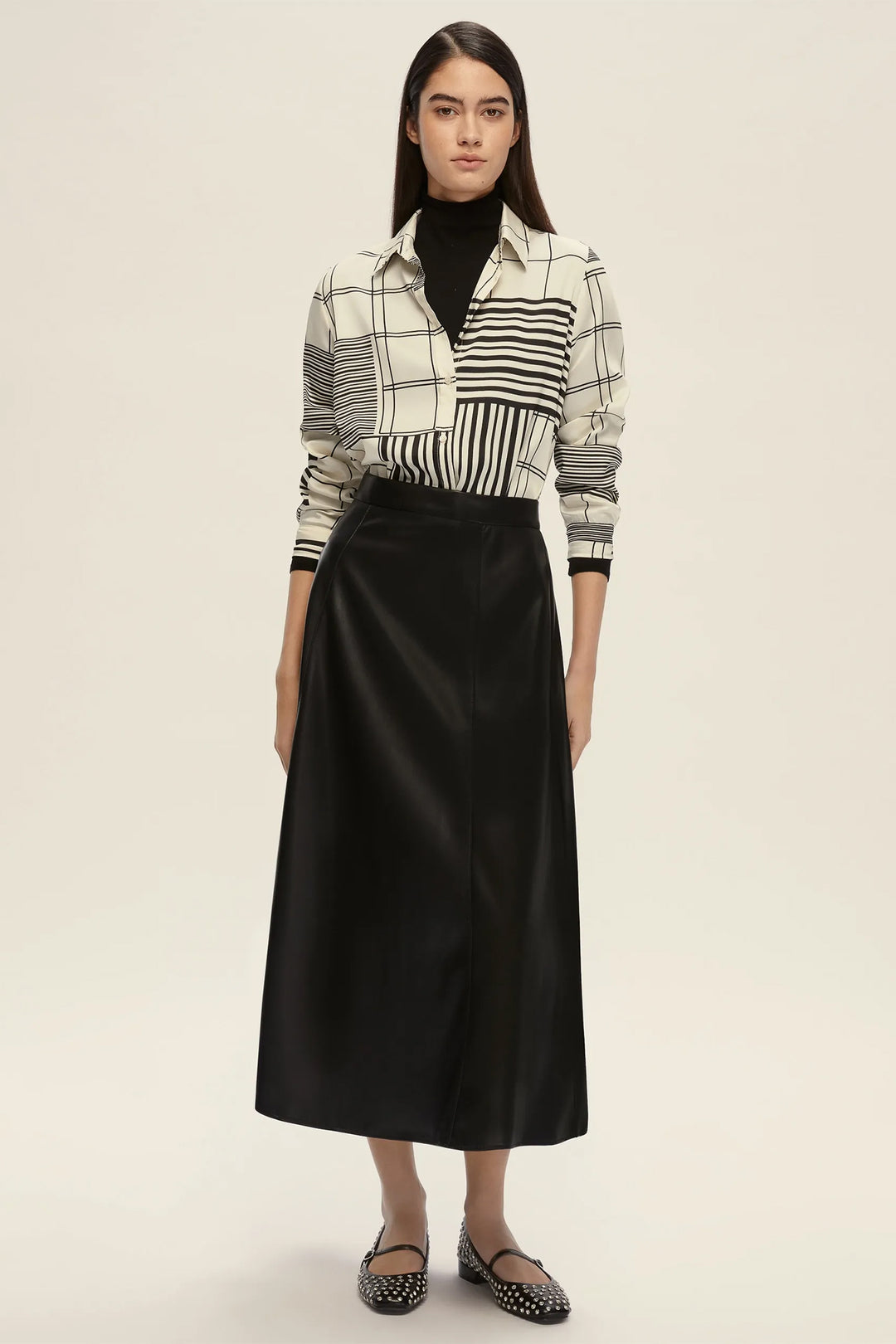 Woman wearing a black and white checkered shirt with a black skirt on a beige background