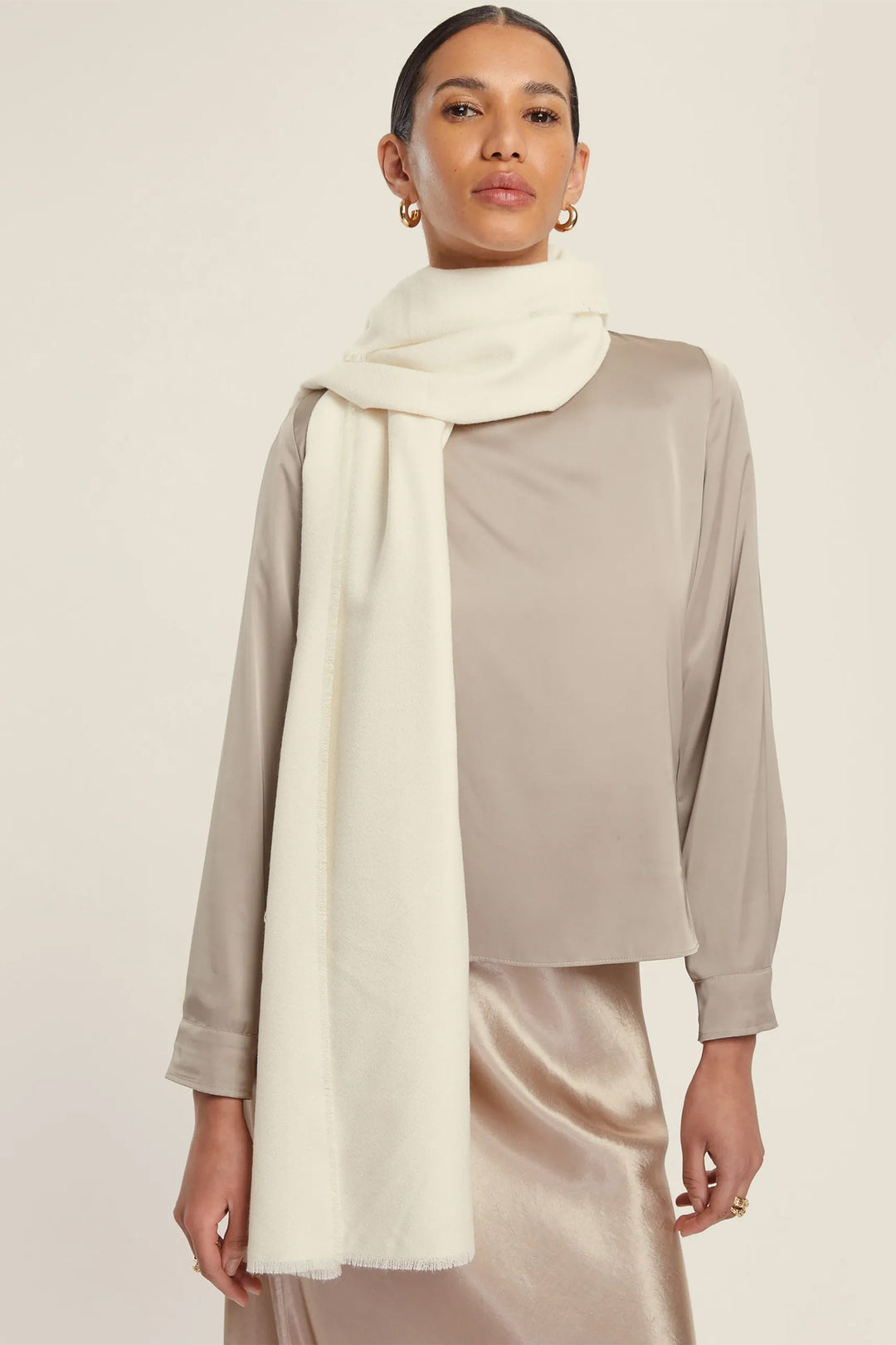 Woman wearing a beige top and cream scarf against a plain background