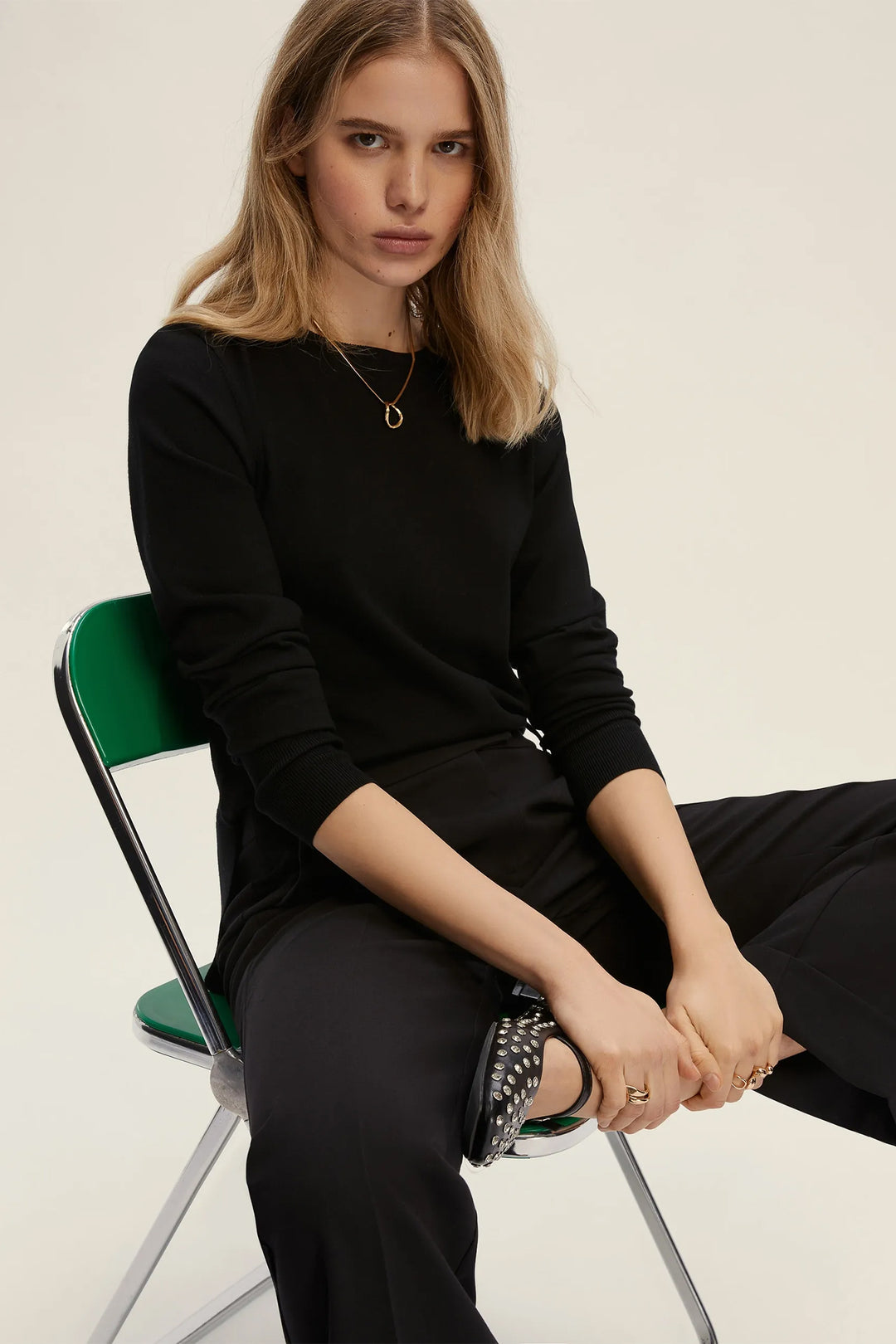 Woman sitting on a green chair wearing a black outfit against a plain background