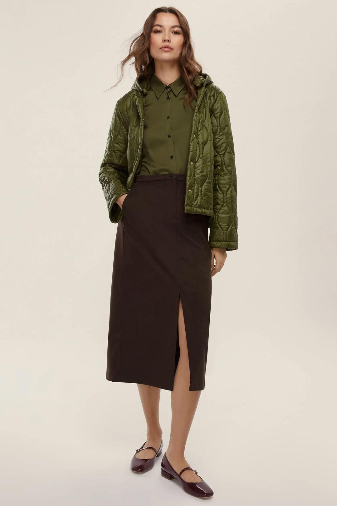 Woman wearing a green jacket over a green shirt and black skirt on a beige background