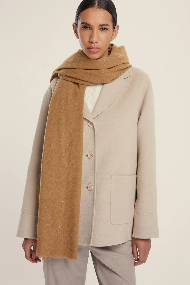 Woman wearing a beige coat and brown scarf on a plain background