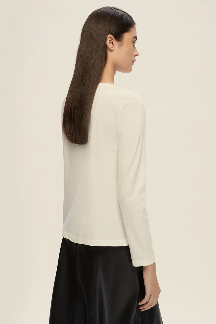 Woman wearing a white long-sleeve top and black pants on a beige background