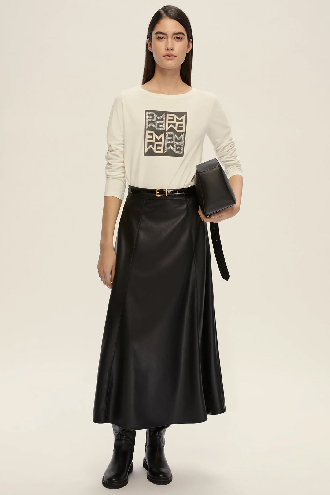 Woman wearing a cream sweater with a logo and a black satin skirt on a beige background