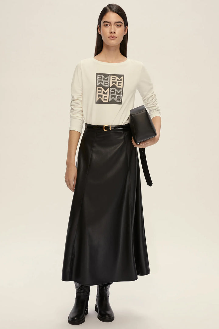 Woman wearing a cream sweater with a logo and a black satin skirt on a beige background