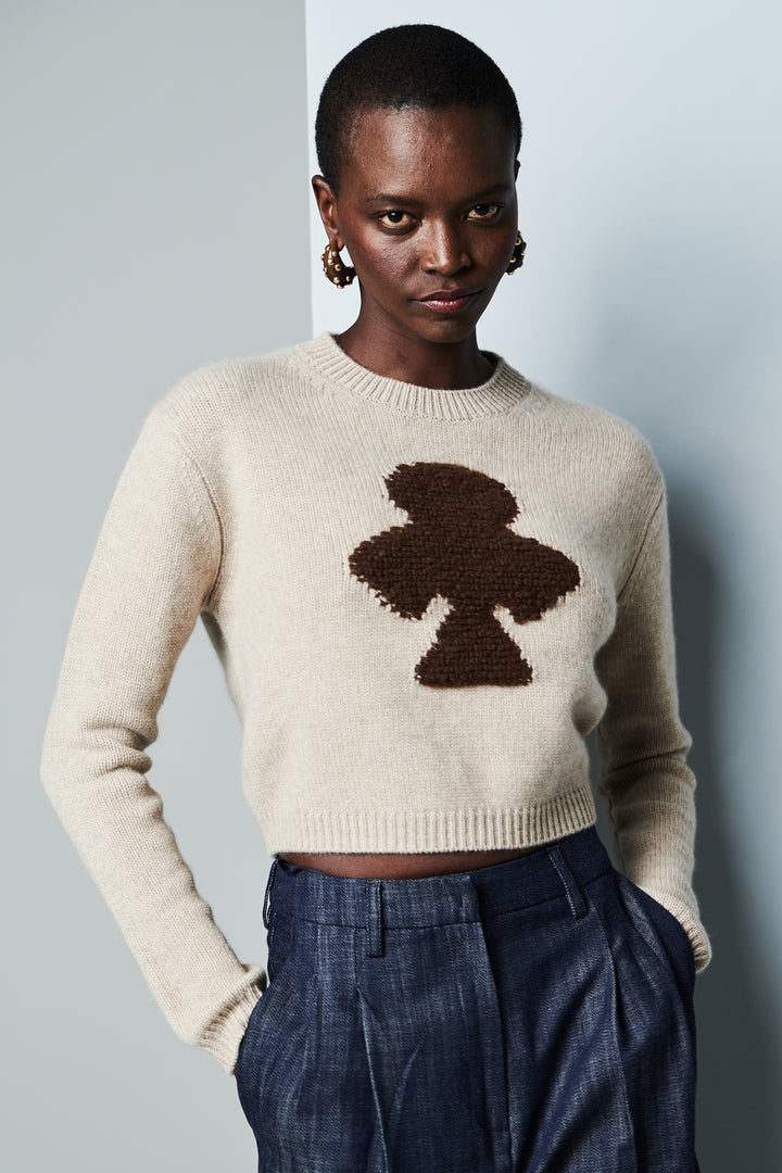 Person wearing a beige sweater with a brown abstract design against a plain background
