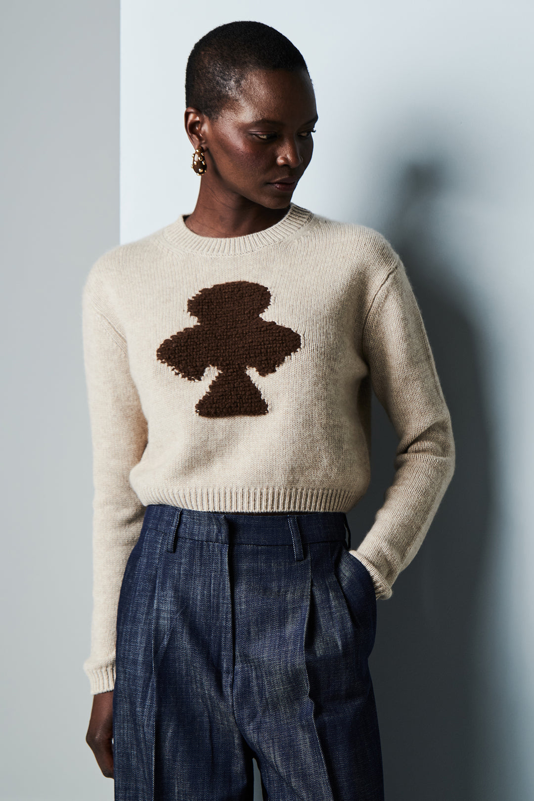Person wearing a beige sweater with a brown abstract design against a plain background