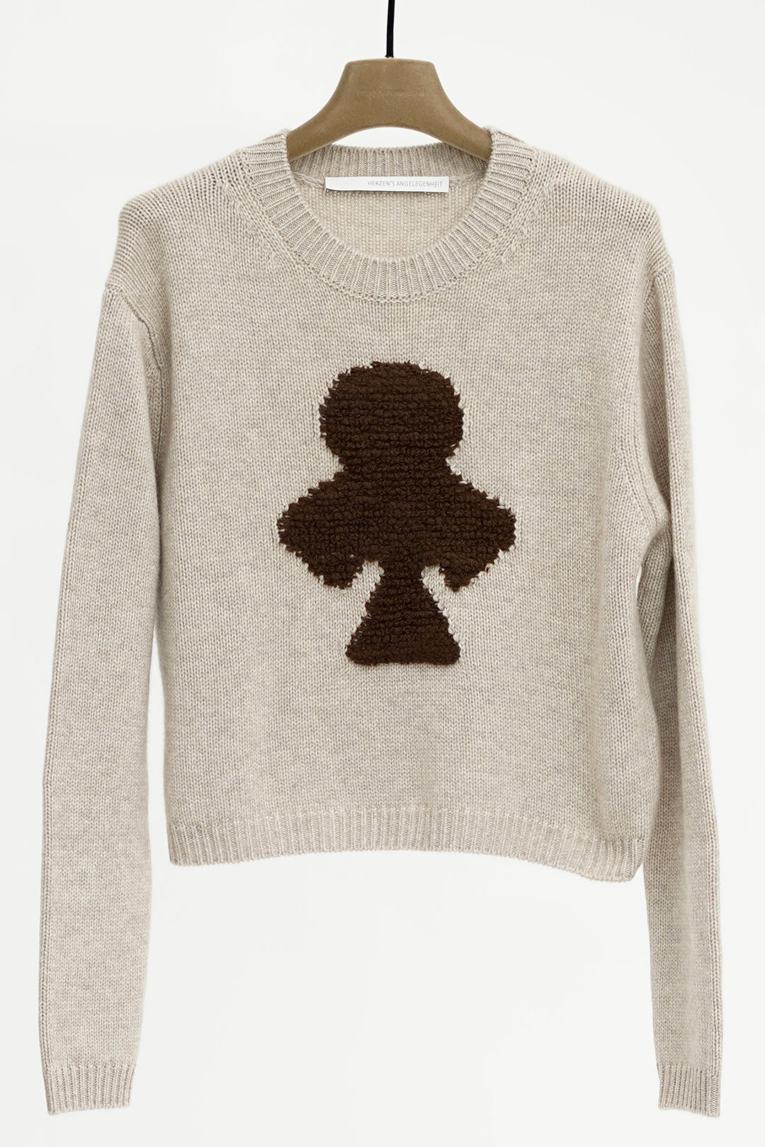 Beige sweater with a black clover design on a hanger against a white background