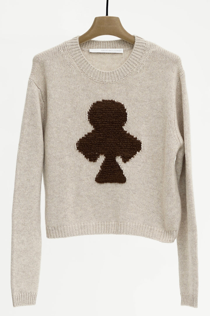 Beige sweater with a black clover design on a hanger against a white background