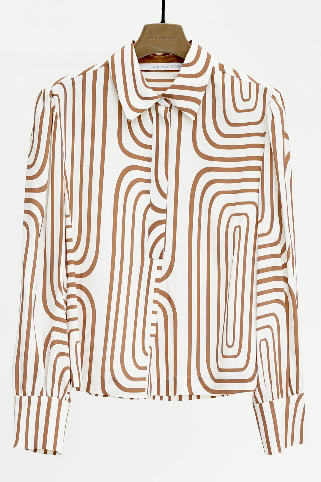 Brown and white patterned blouse on a hanger against a white background