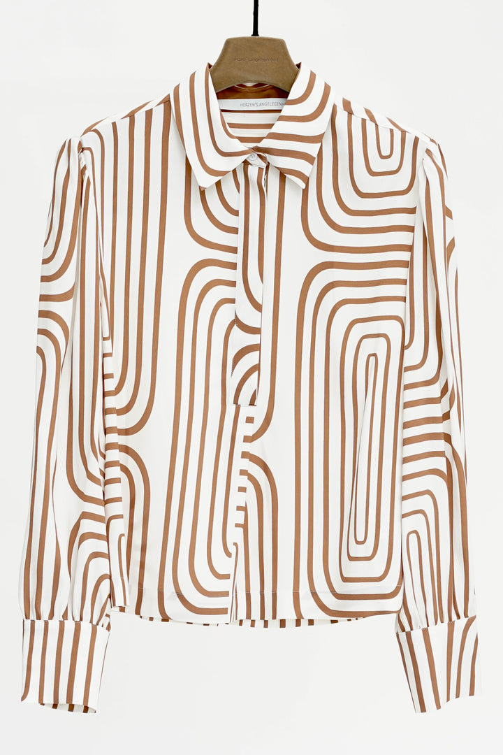 Brown and white patterned blouse on a hanger against a white background