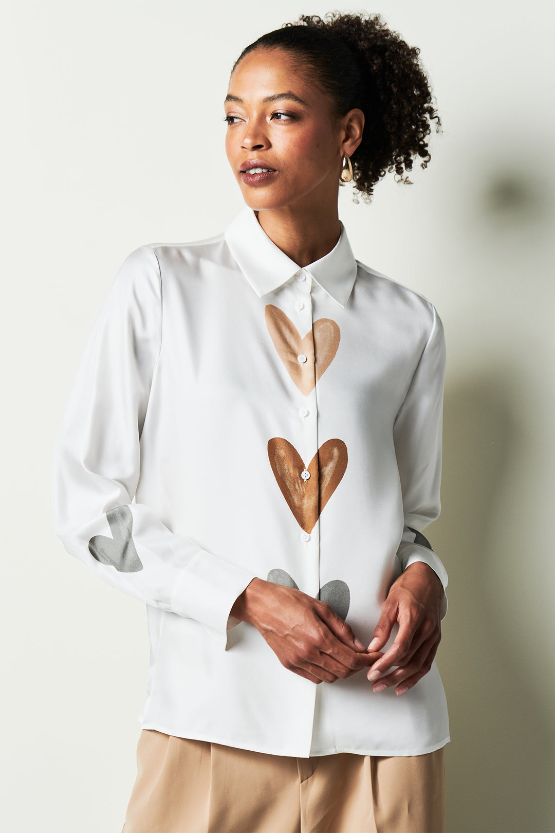 Woman wearing a white shirt with heart designs on a plain background