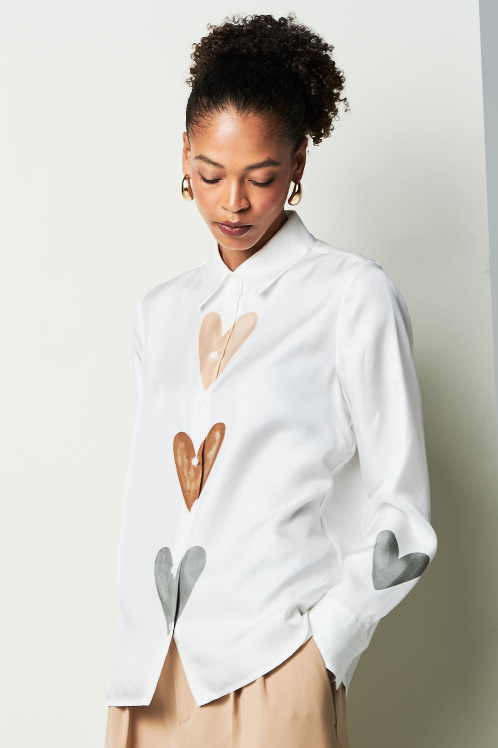 Woman wearing a white shirt with heart designs on a plain background