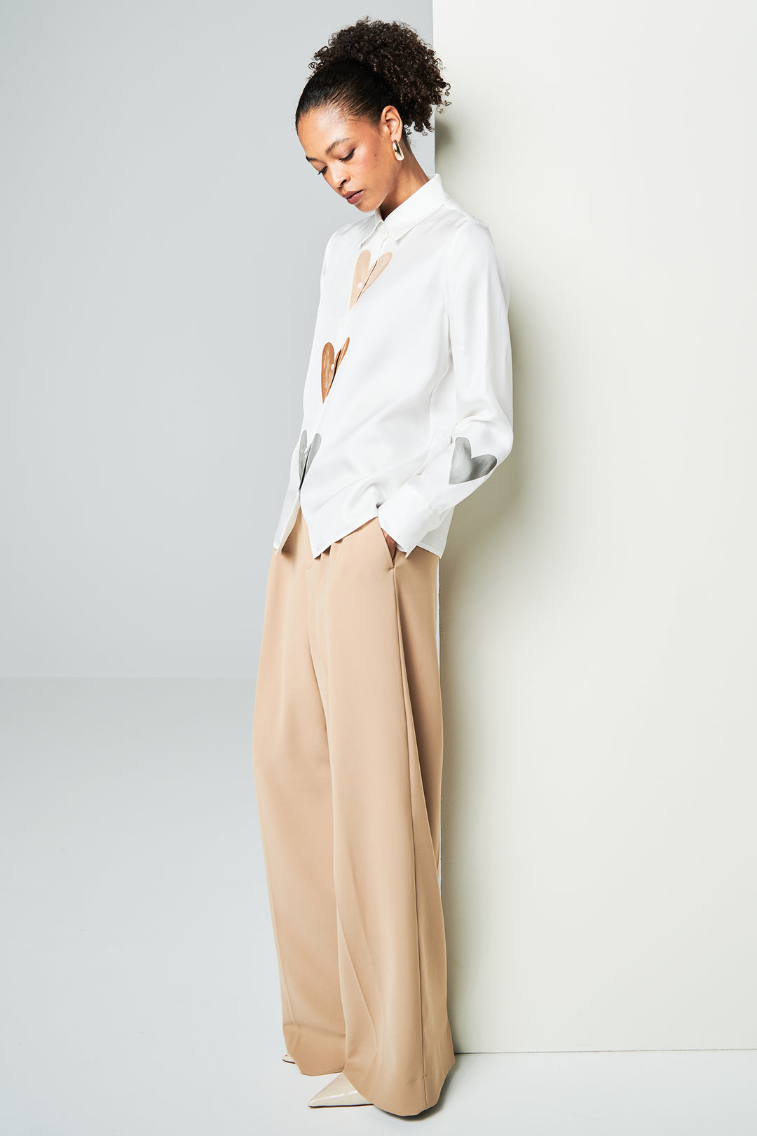 Woman wearing a white blouse and beige pants against a white wall