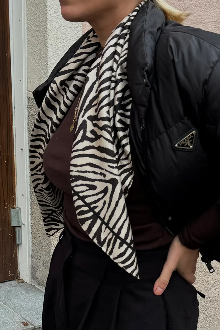 Person wearing a zebra print scarf and black jacket against a neutral wall.