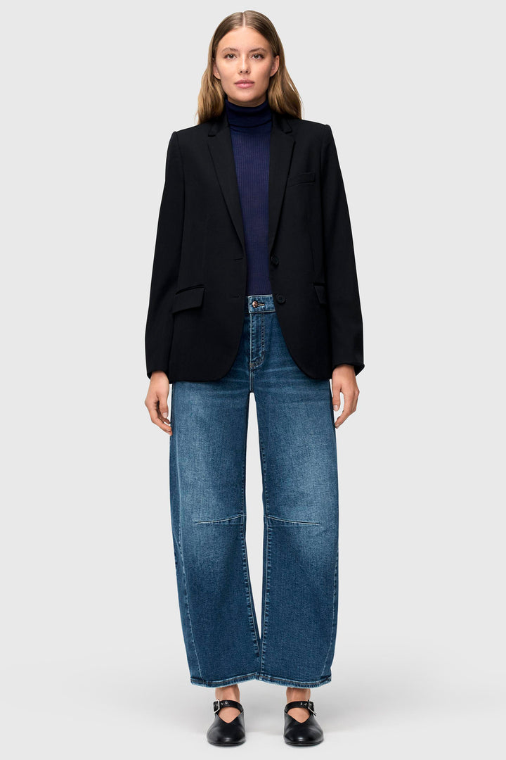 Woman wearing a black blazer, navy turtleneck, and blue jeans on a white background