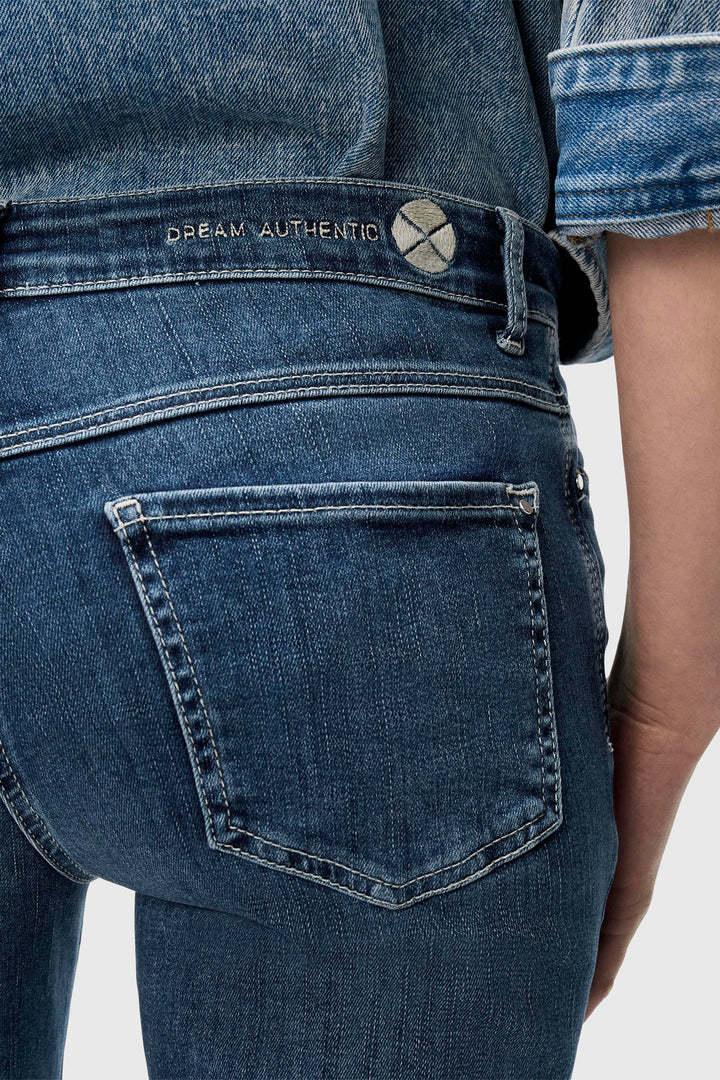 Close-up of blue jeans with a visible brand logo on a light gray background