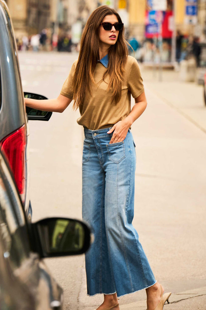 Woman in a beige top and blue jeans getting into a car on a city street.