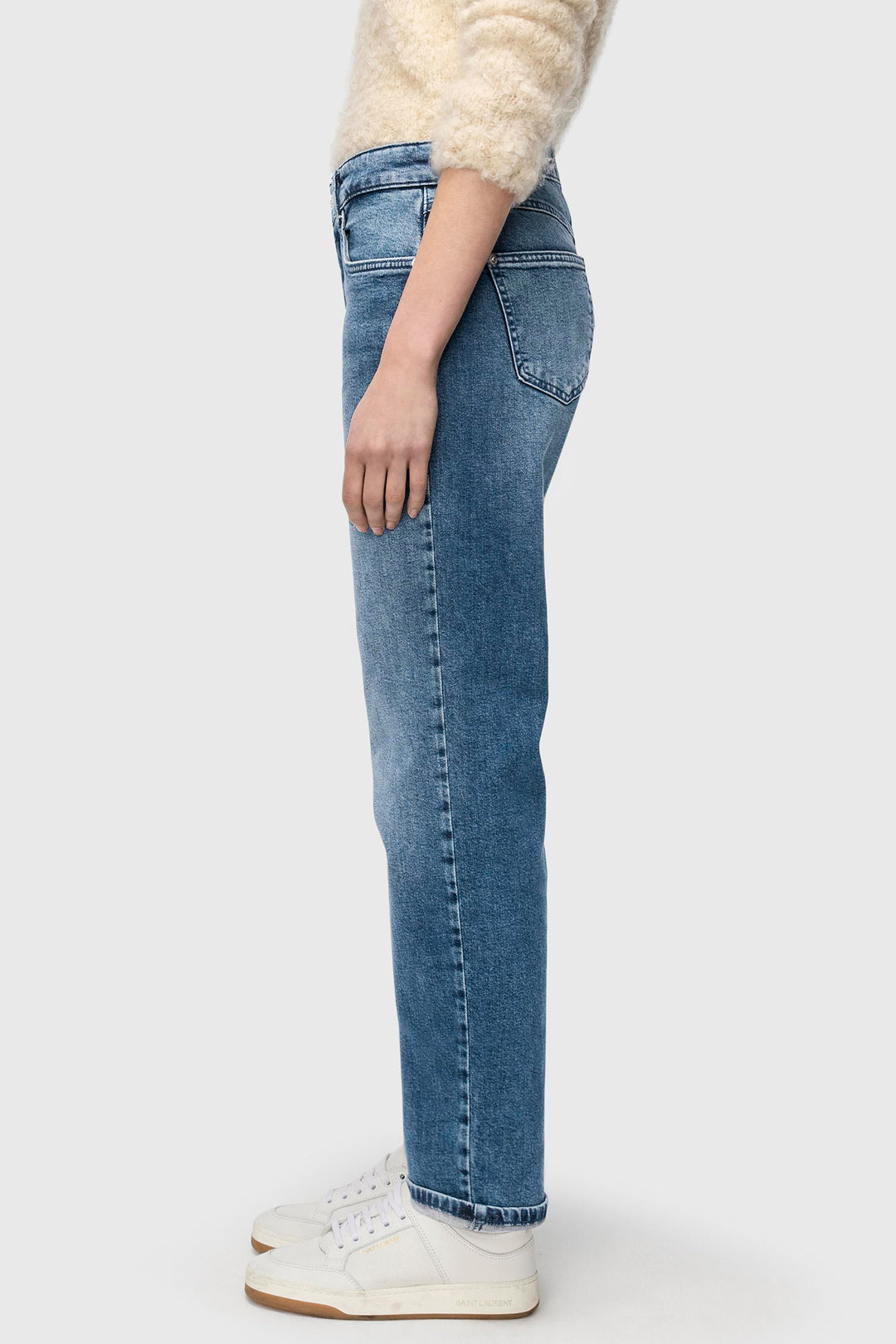 Person wearing blue jeans and a cream sweater on a white background