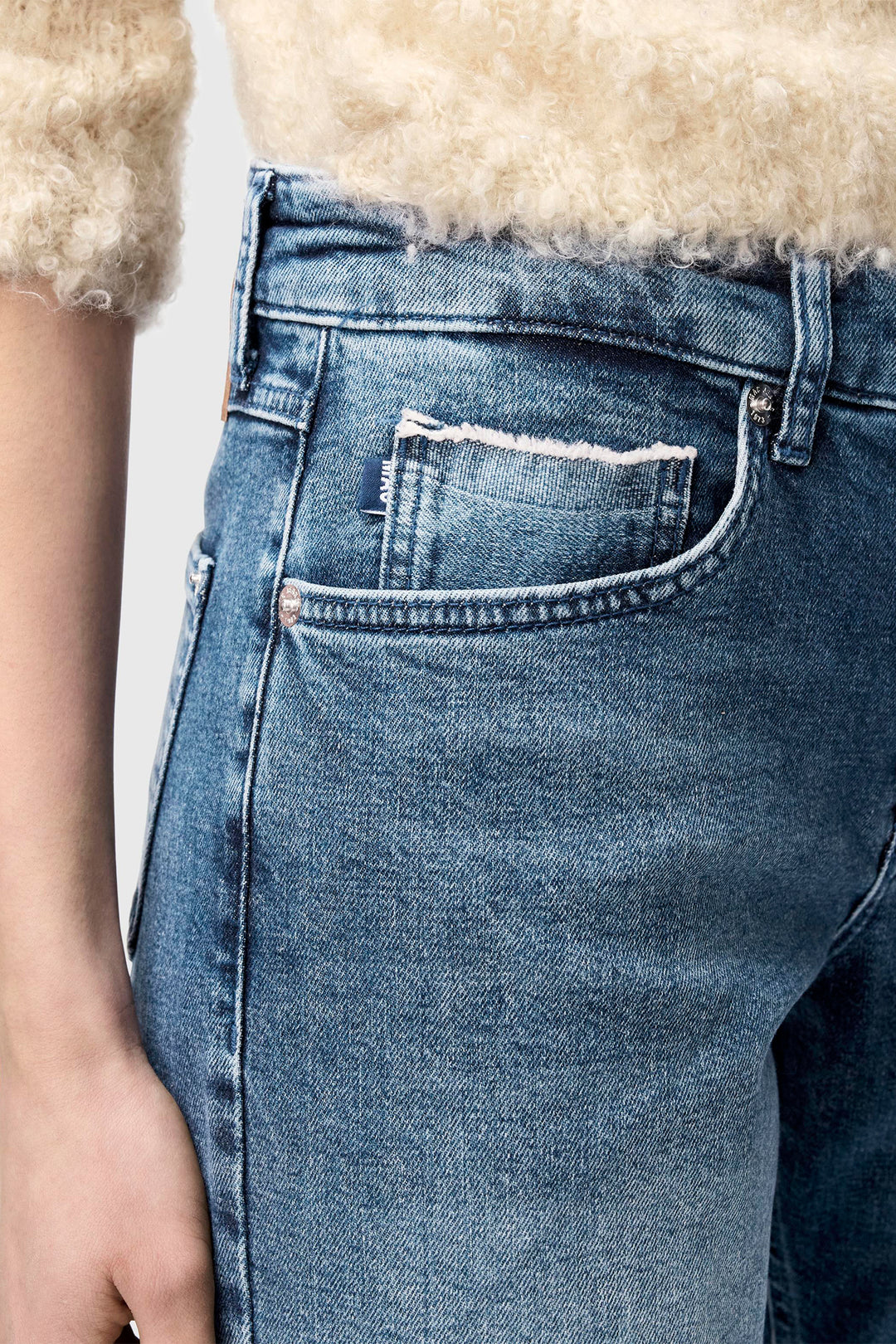 Close-up of blue jeans with a brand label on the pocket against a neutral background