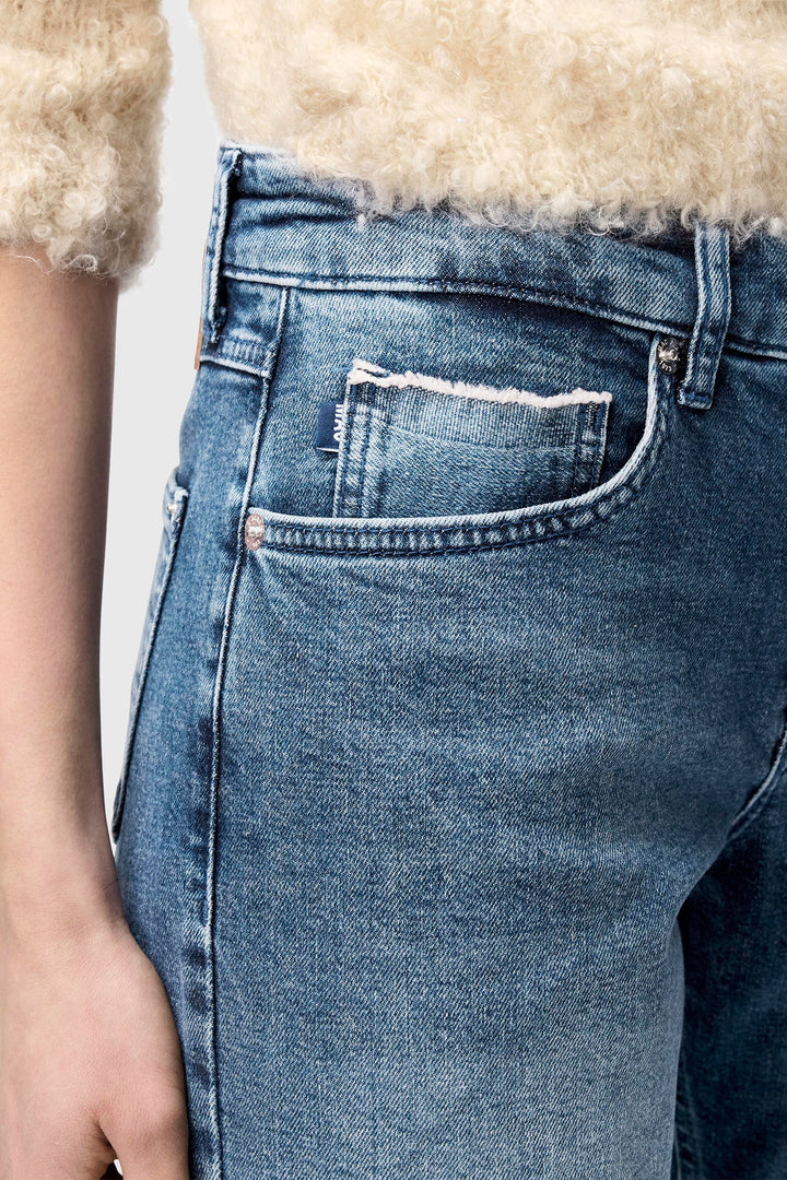 Close-up of blue jeans with a brand label on the pocket against a neutral background