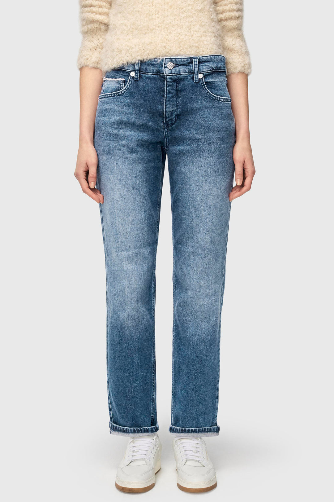 Person wearing blue jeans and a beige sweater on a white background