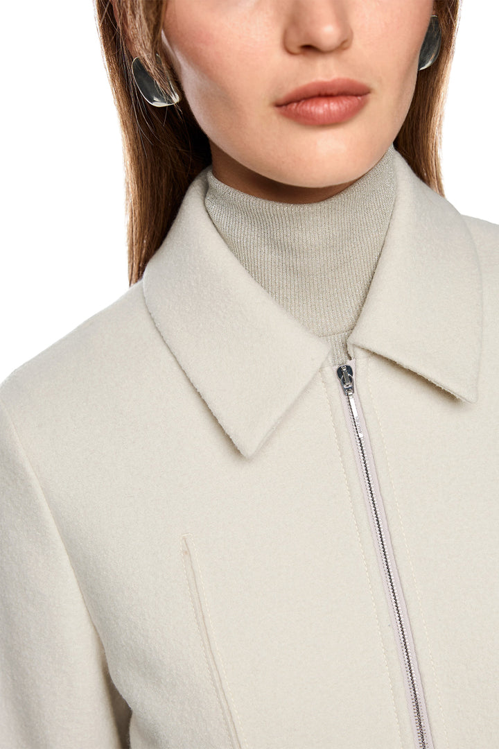 Close-up of a person wearing a light gray coat with a high collar and zipper.