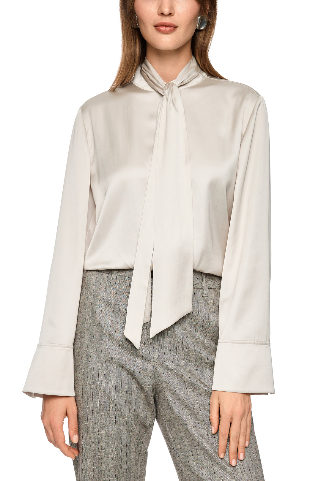 Woman wearing a light beige blouse with a tie detail and gray checkered pants on a white background