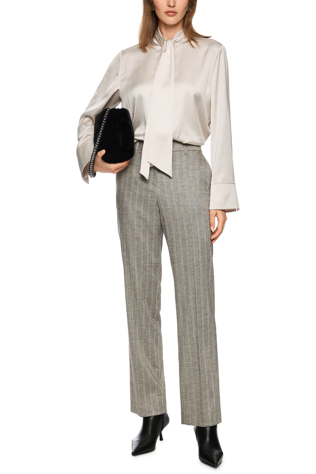 Woman wearing a white blouse with a bow tie and gray checkered pants, holding a black clutch.