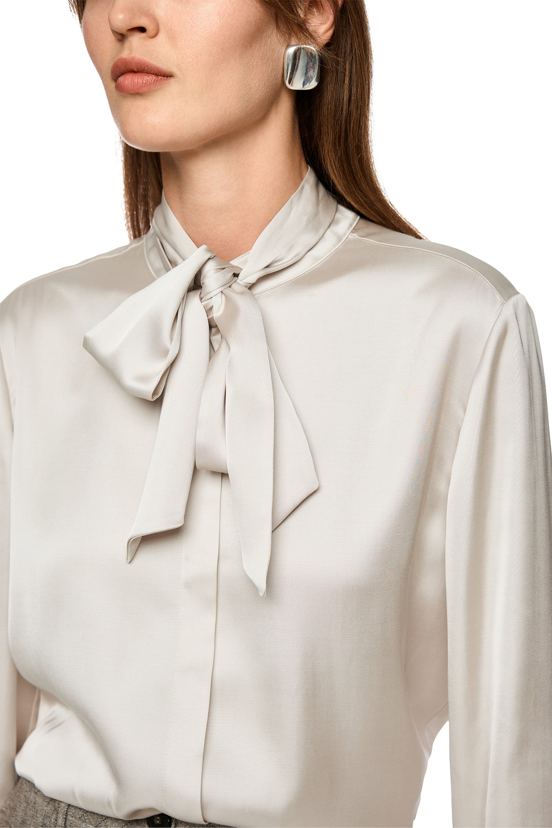 Close-up of a person wearing a beige blouse with a bow detail.