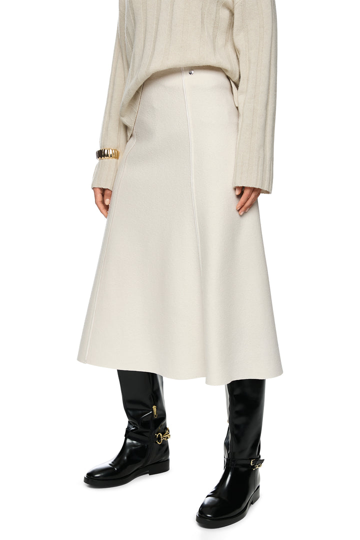 Person wearing a beige coat, white skirt, and black boots on a white background