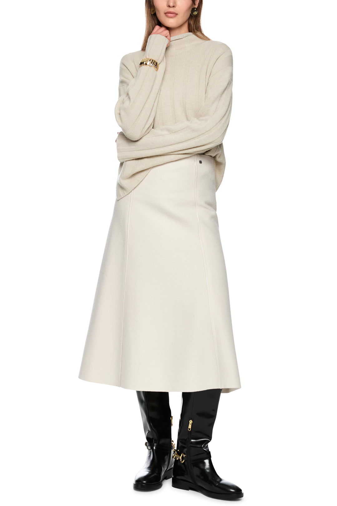 Person wearing a beige sweater and skirt with black boots on a white background