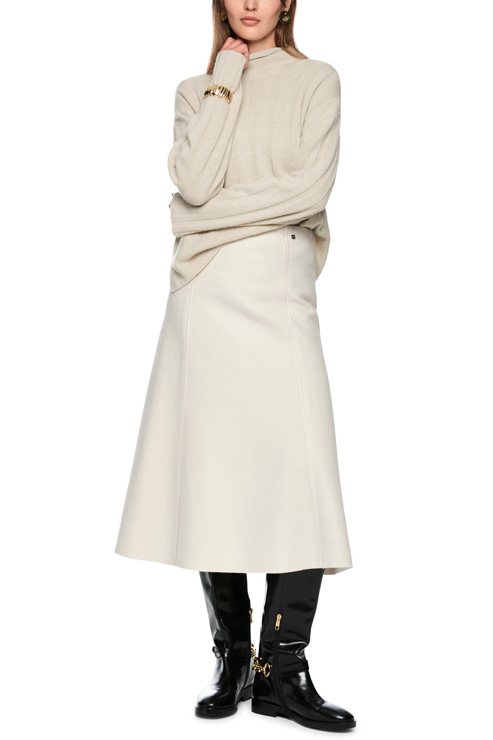 Person wearing a beige sweater and skirt with black boots on a white background