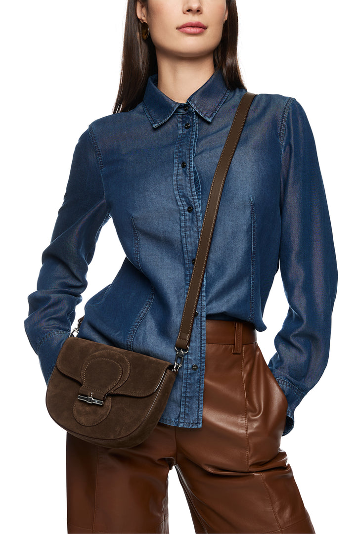 Woman wearing a blue shirt and brown leather pants with a brown bag on a white background