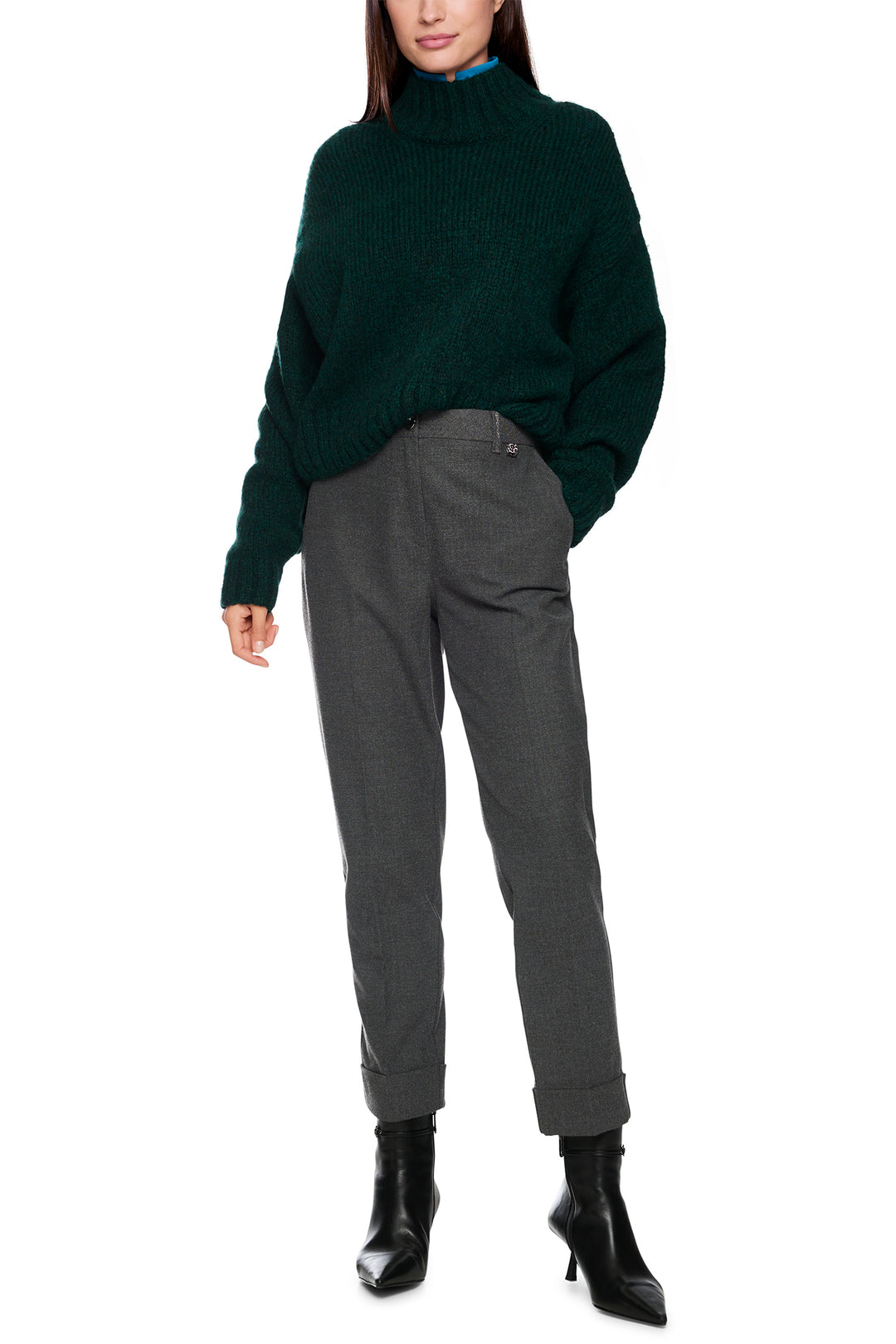 Person wearing a dark green sweater and gray pants on a white background