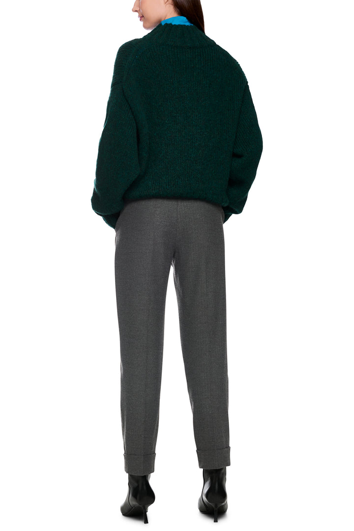 Person wearing a green sweater and gray pants on a white background