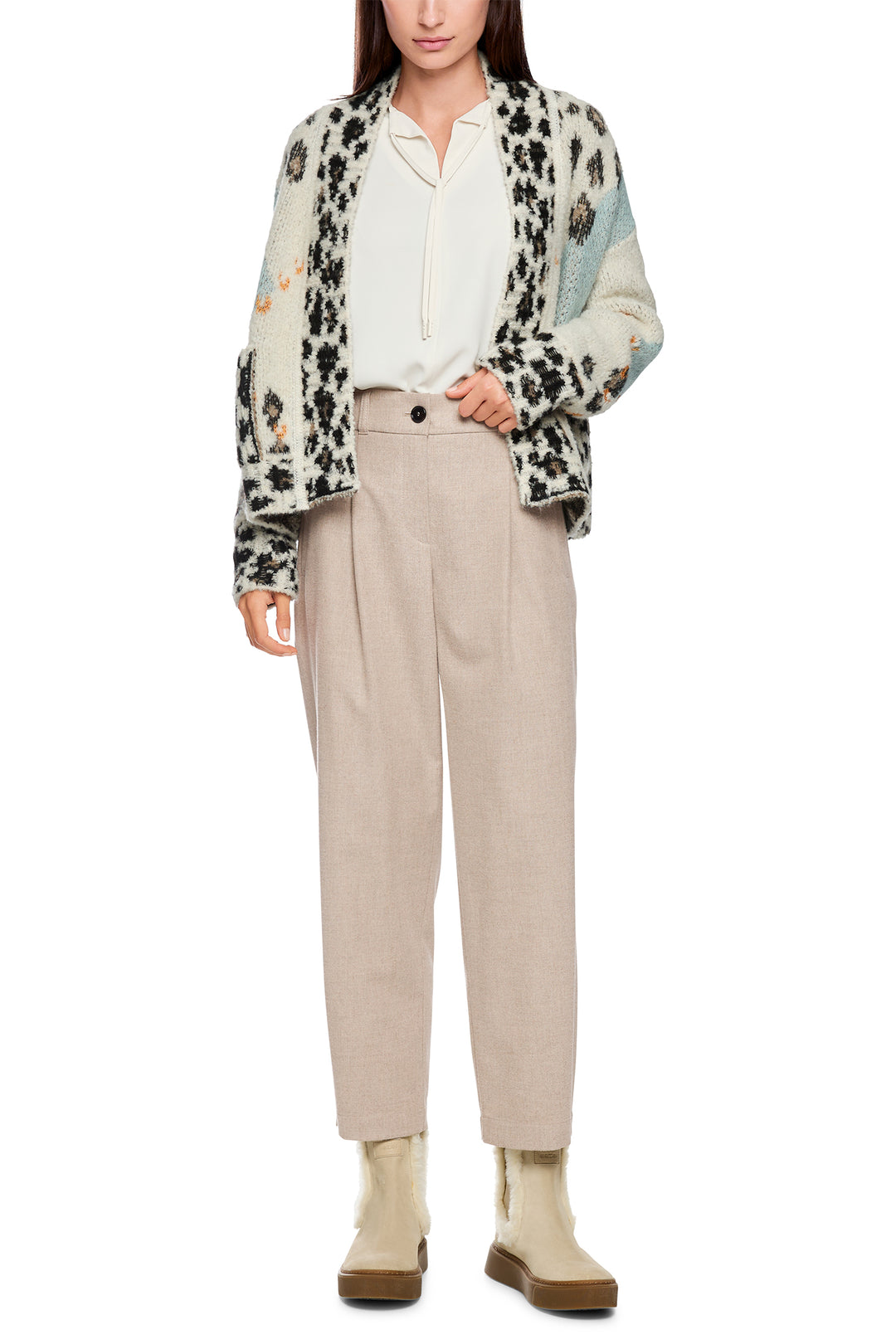 Woman wearing a patterned jacket, white shirt, beige pants, and beige shoes on a white background