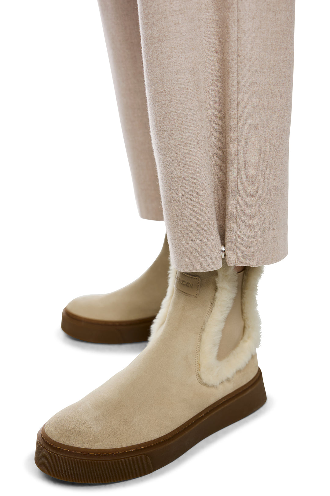 Beige boots with brown soles worn with beige pants on a white background