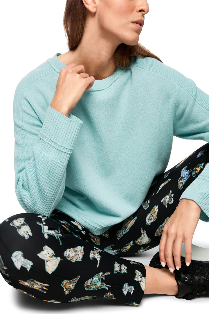 Woman wearing a light blue sweater and black pants with animal print sitting on a white surface.