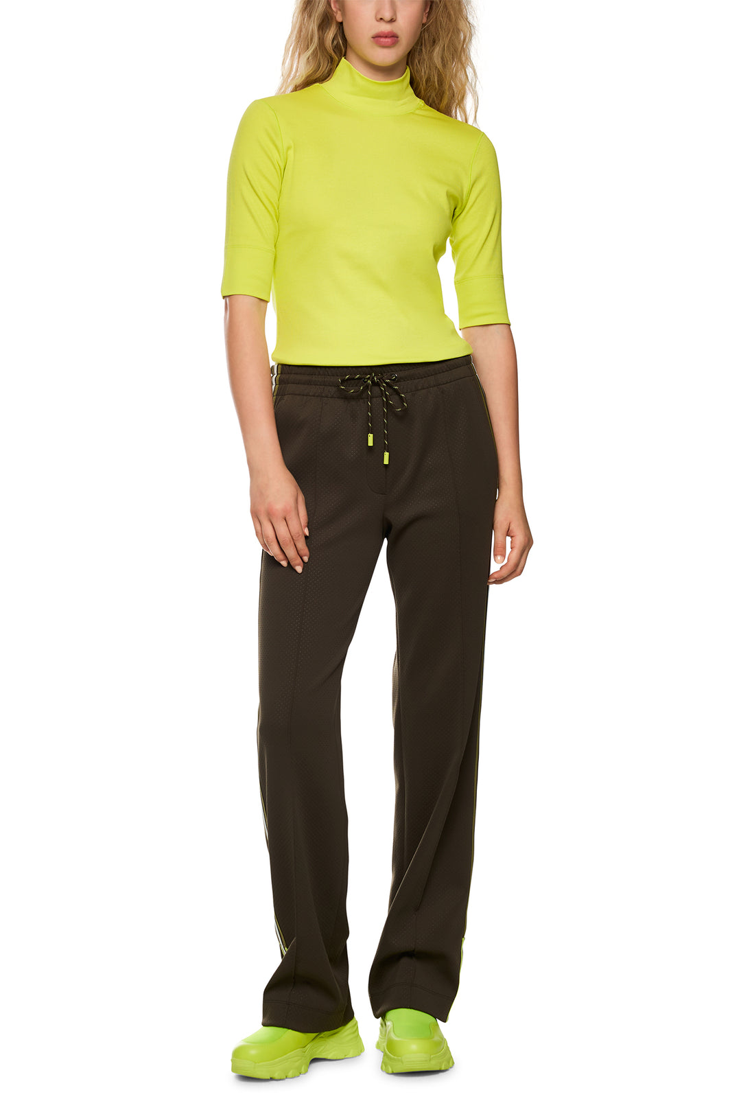 Person wearing a bright green top and brown pants on a white background