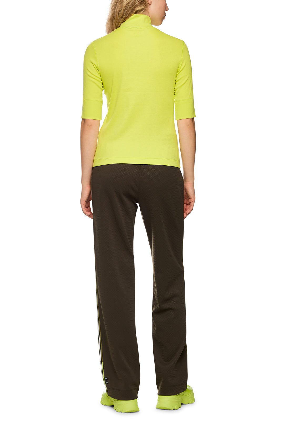 Person wearing a bright green top and black pants on a white background