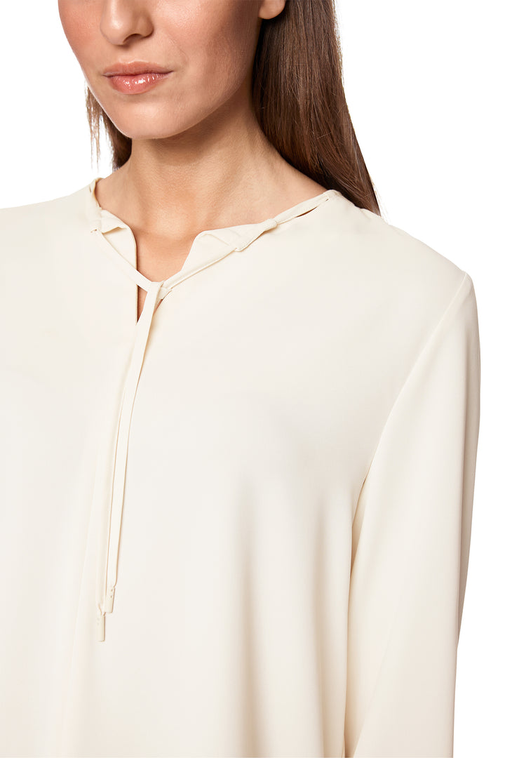 Close-up of a person wearing a cream-colored blouse with a plain background