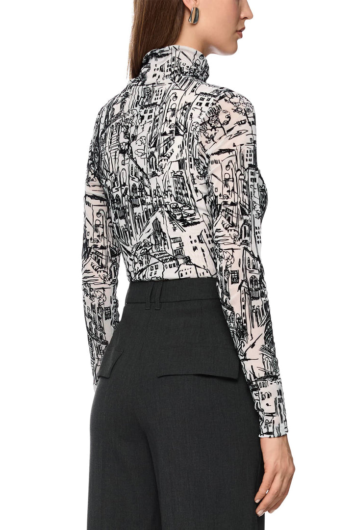 Person wearing a patterned blouse with long sleeves and black pants on a white background